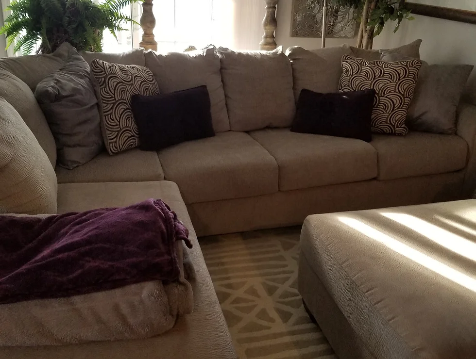 Beige sectional sofa with pillows and ottoman.